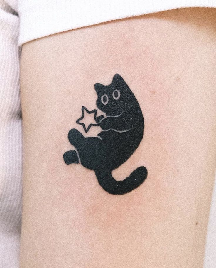 a black cat holding a star tattoo on the right side of the thigh, it's paw