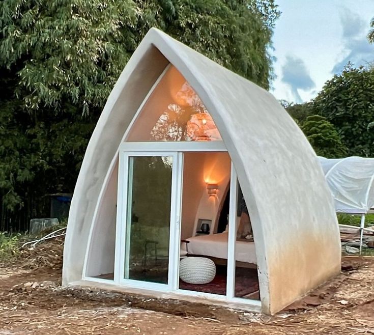 a house made out of concrete sitting on top of a dirt field with trees in the background