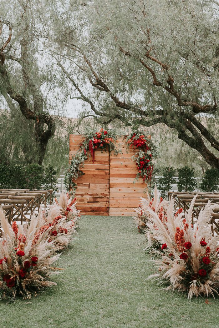 an outdoor ceremony setup with red flowers and pamodia in the foreground, surrounded by greenery