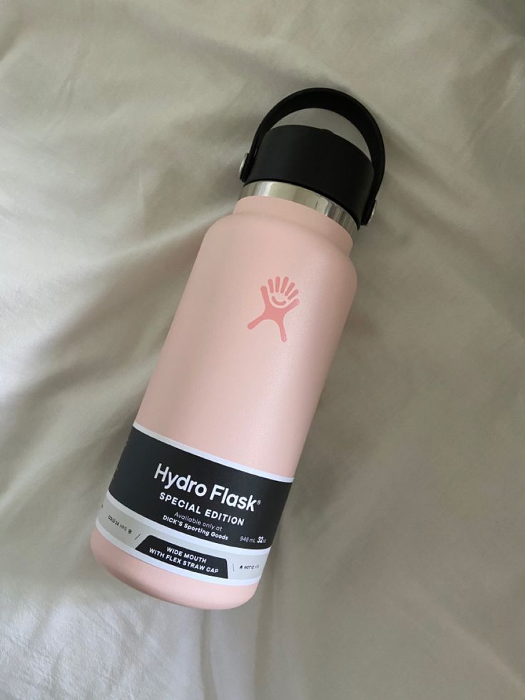 a pink hydro flask water bottle laying on a white bed with a black lid