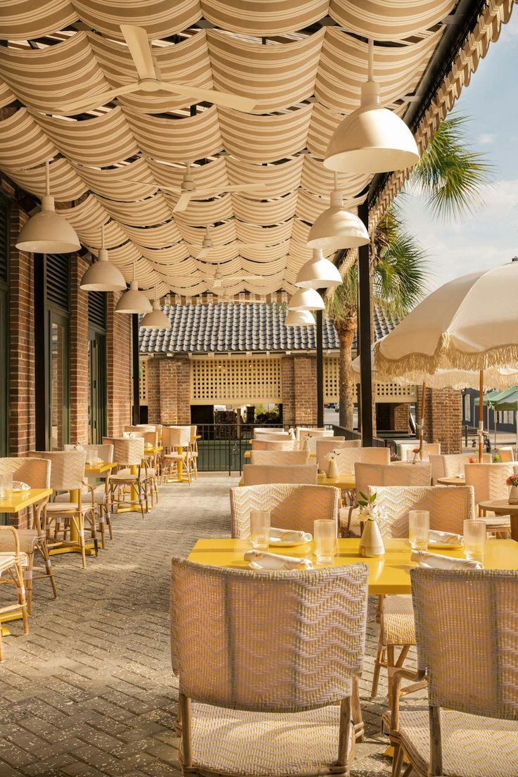 an outdoor dining area with yellow tables and white umbrellas on the roof over looking the water