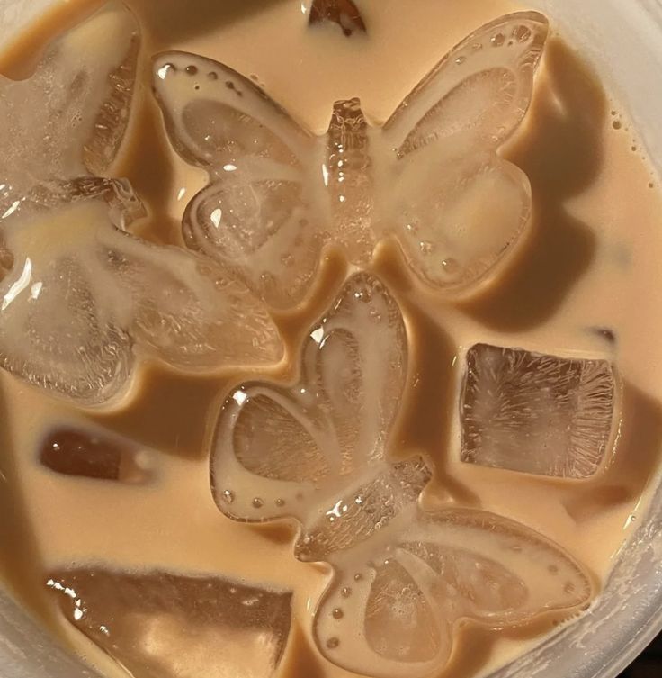 some ice cubes are sitting in a bowl with liquid on top and butterflies above them