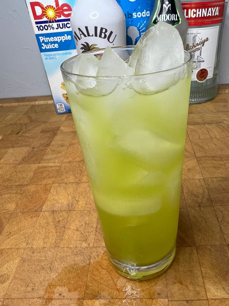 a green drink sitting on top of a wooden table next to bottles of soda and ice