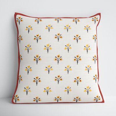 a white pillow with yellow and red flowers on the front, sitting against a wall