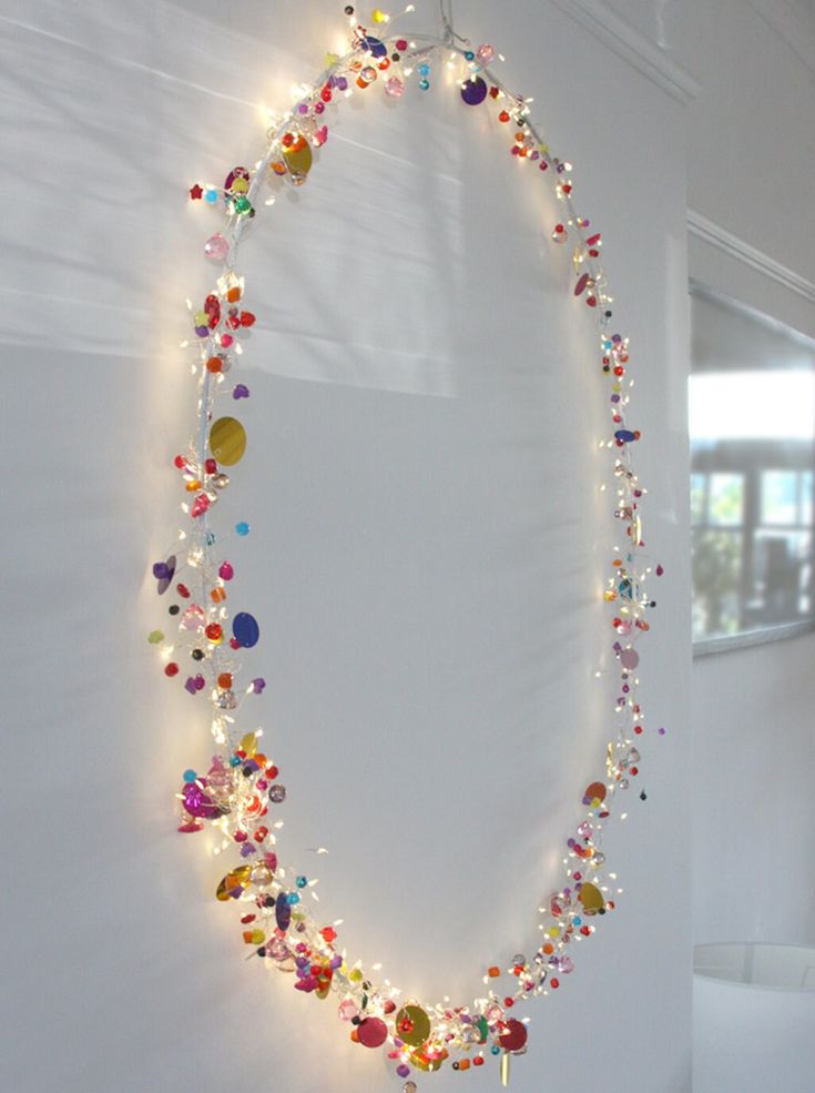 a necklace is hanging on the wall with lights around it and beads all over it