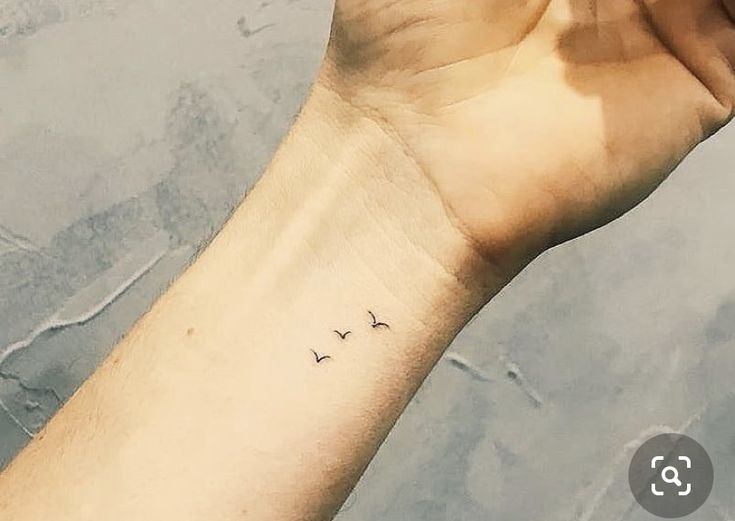 a person's arm with a small bird tattoo on the left side of their wrist