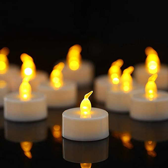 many lit candles sitting on top of a black surface with reflections in the water around them