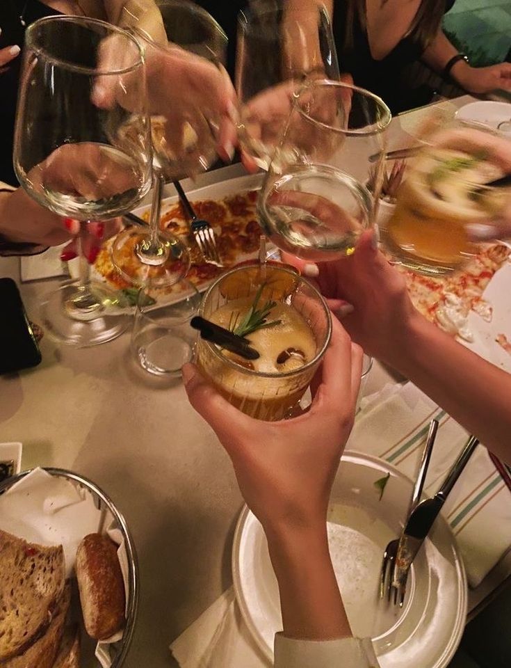 several people are holding wine glasses at a table with food and drinks on it,