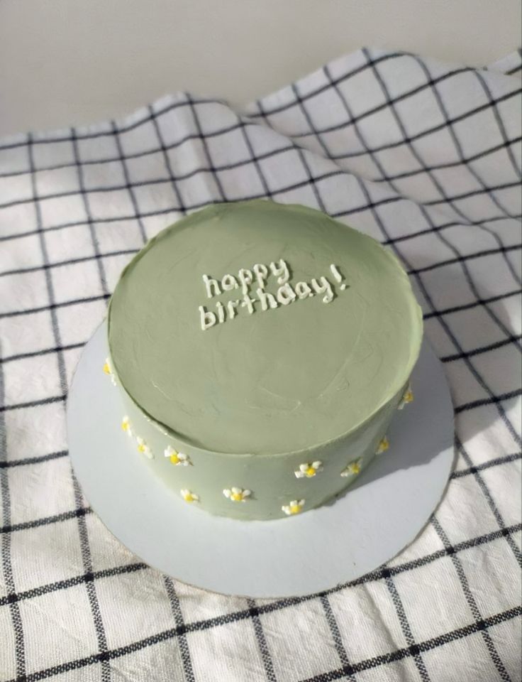 a green birthday cake sitting on top of a white and black checkered table cloth