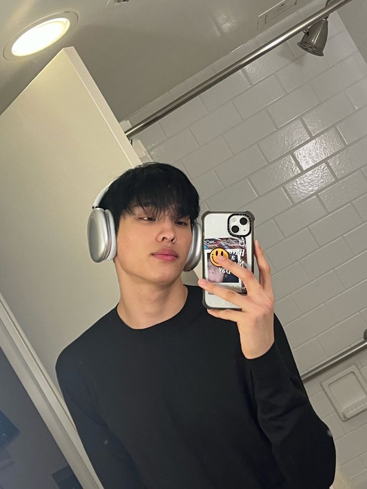 a man wearing headphones taking a selfie in the mirror with his cell phone