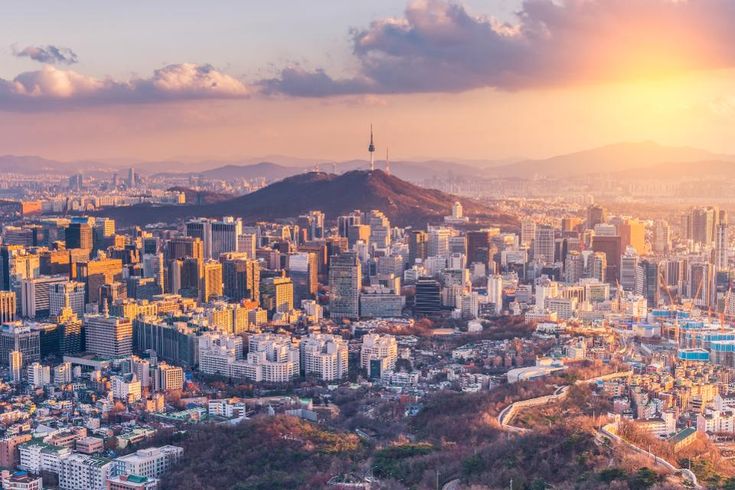 an aerial view of a city with tall buildings and mountains in the background at sunset