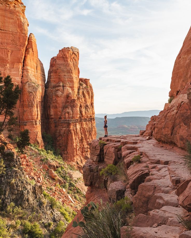 a man standing on top of a rocky cliff next to tall red rocks and trees