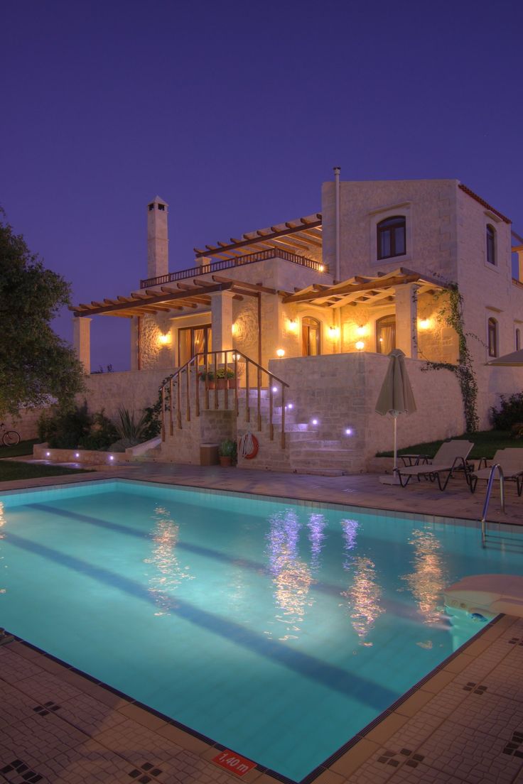 an empty swimming pool in front of a house at night with lights on the windows