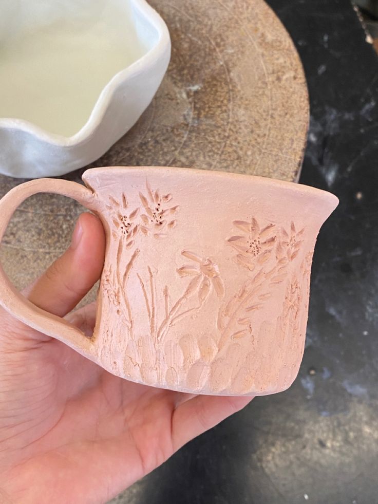 a hand holding a pink vase with flowers on it and a bowl in the background