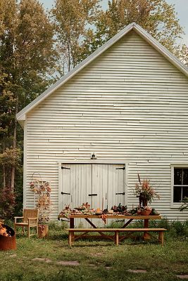 an old white building with a picnic table in front of it and autumn decorations on the outside