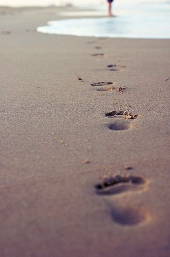 two people walking on the beach with footprints in the sand