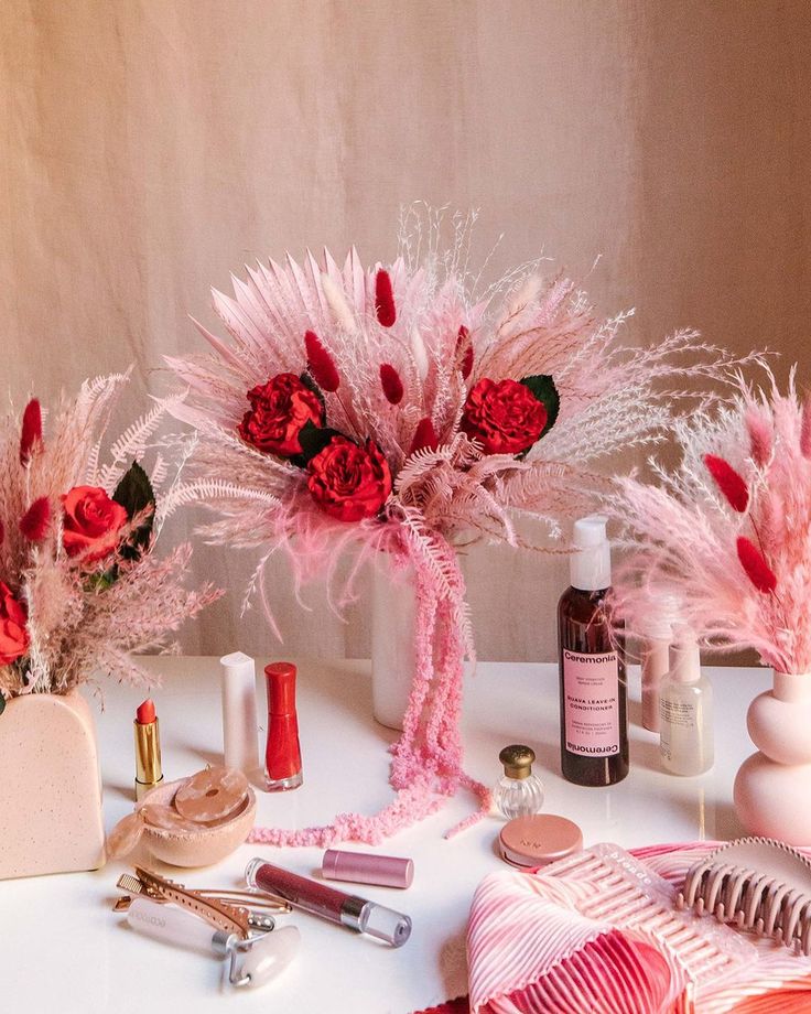 the table is covered with pink and red flowers, lipstick, perfume bottles, and other decorative items