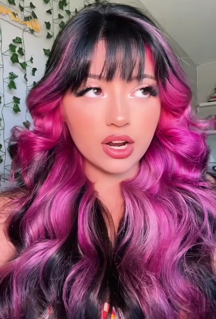 a woman with pink and black hair is making a funny face while wearing long wavy purple hair