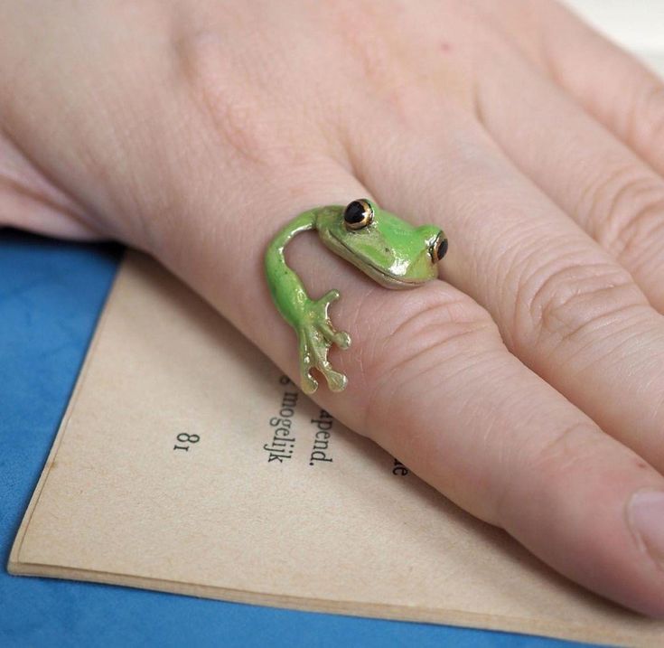 a green frog ring sitting on top of a person's hand next to a piece of paper