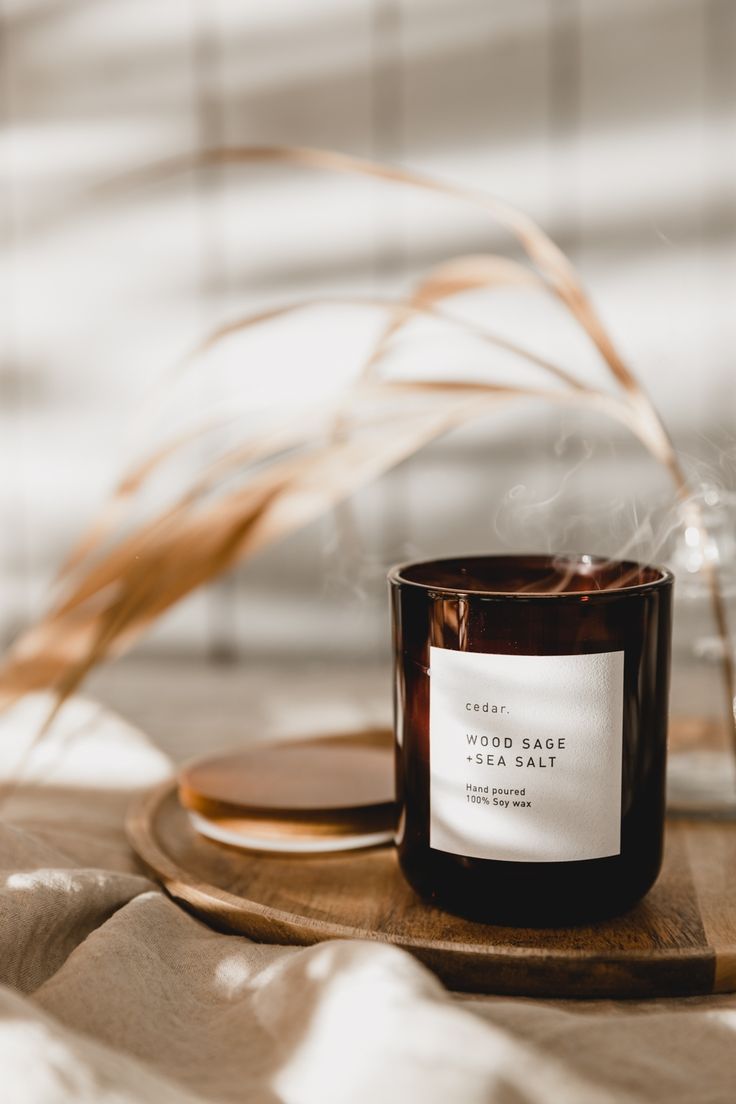 a candle sitting on top of a wooden tray next to a glass bottle and some dry grass