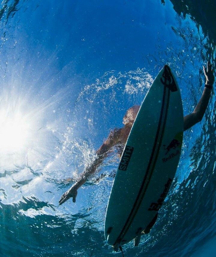 a man is swimming in the ocean with his surfboard under water and sun shining