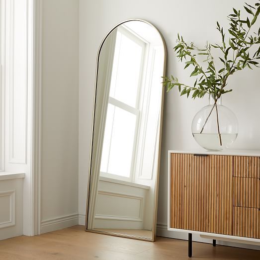 a mirror sitting on top of a wooden floor next to a vase with a plant in it