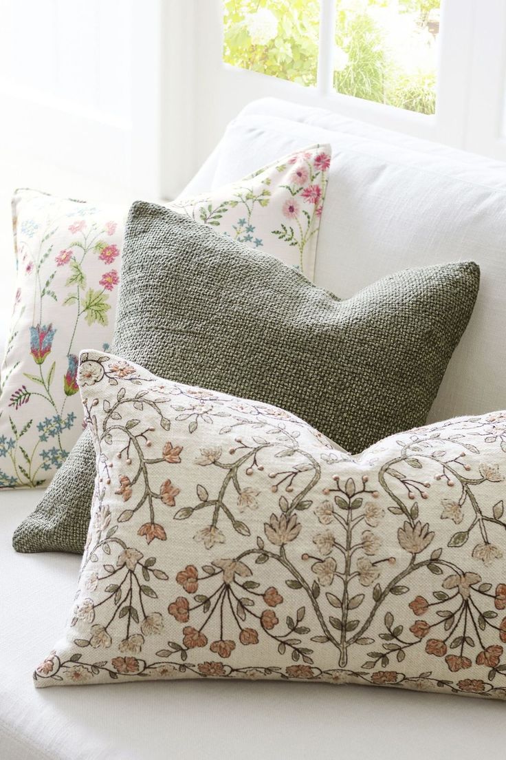 pillows on a white couch in front of a window with green and pink floral designs