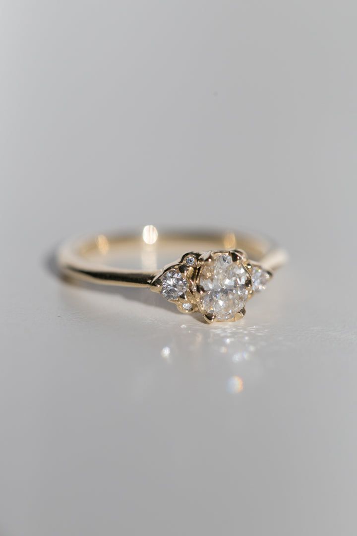 Elegant. Dainty. Classic. The Lily of the Valley ring is a hand-carved cluster ring, with a vintage inspired 6 prong setting around the center stone. This design features a 6x4mm oval centerstone (roughly .37ct), complimented with six recycled diamonds (approximately .11ctw). The solid gold setting has a 1.7mm band, and tapers slightly where it meets the stones. Want to customize this ring with your choice of gems? Contact us with a special request. Made-to-order, please leave your size in the n Oval Rose Cut Diamond Promise Ring, Timeless Cluster Ring With Rose Cut Diamonds For Wedding, Timeless Wedding Cluster Ring With Rose Cut Diamonds, Timeless Rose Cut Diamond Cluster Ring For Wedding, Timeless 14k Gold Cluster Anniversary Ring, Timeless 14k Gold Cluster Ring For Anniversary, Cluster Ring With Rose Cut Diamonds For Promise, Wedding Cluster Ring With Center Stone In 14k Gold, Heirloom 14k Gold Cluster Ring With Round Cut