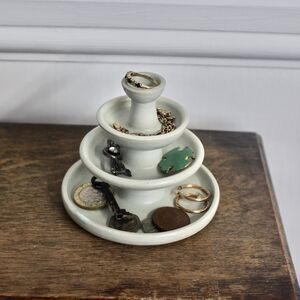 three tiered tray with rings and other items on it sitting on top of a wooden table