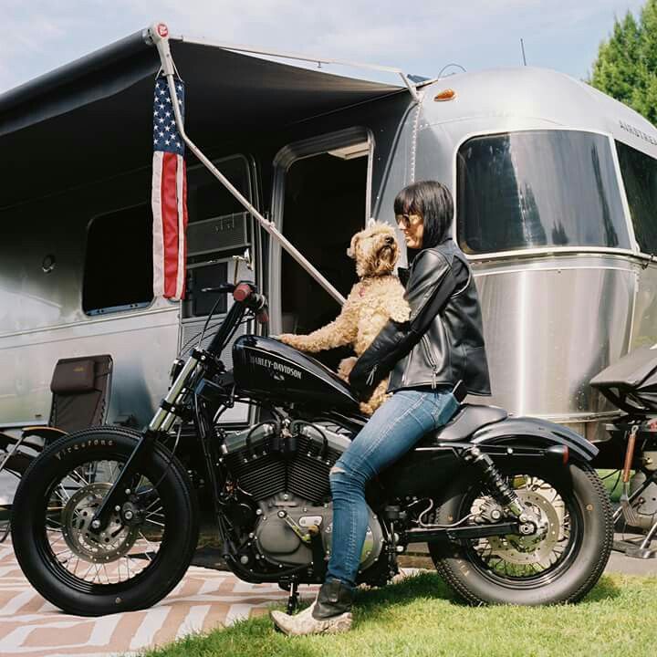 a woman sitting on a motorcycle with her dog in front of an airshow trailer