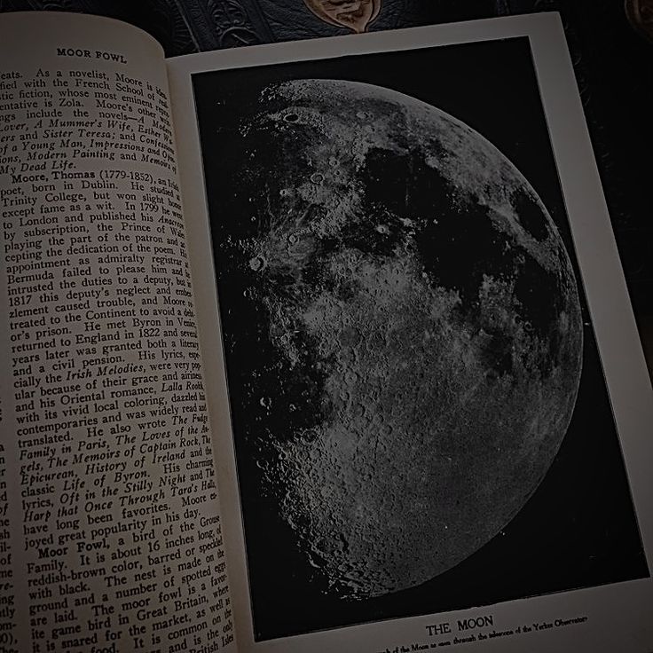 an open book with the moon on it's cover and some writing in front of it