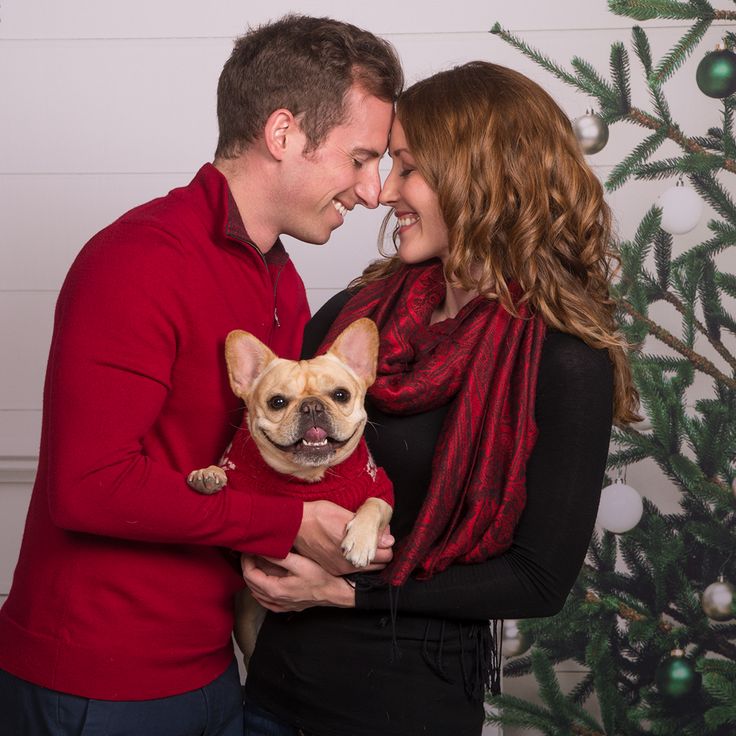 a man and woman holding a dog in front of a christmas tree