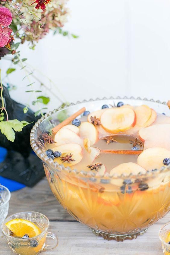 a glass bowl filled with fruit on top of a table next to glasses and flowers