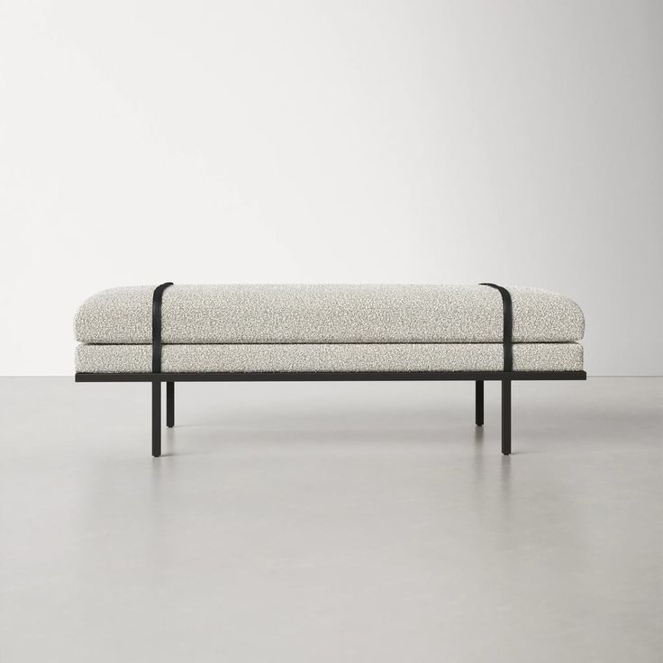 an upholstered bench with black metal legs and a light colored fabric cover on the back