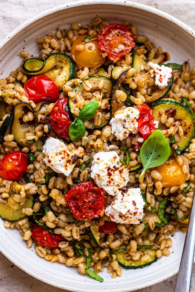 a white bowl filled with farro salad on top of a table next to a fork