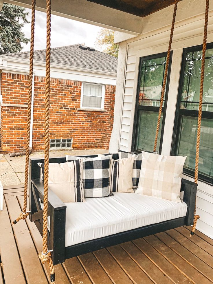 a black and white porch swing bed with pillows on it's back end, in front of a brick building