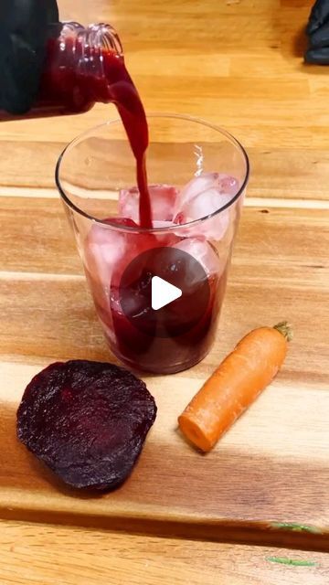 a person pouring red wine into a glass with carrots and beets on the side