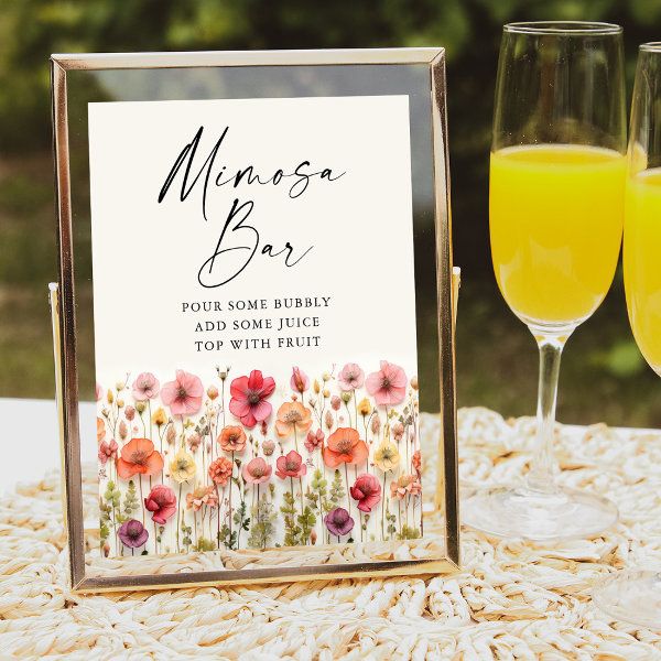 two glasses of champagne and a sign on a table with flowers next to each other