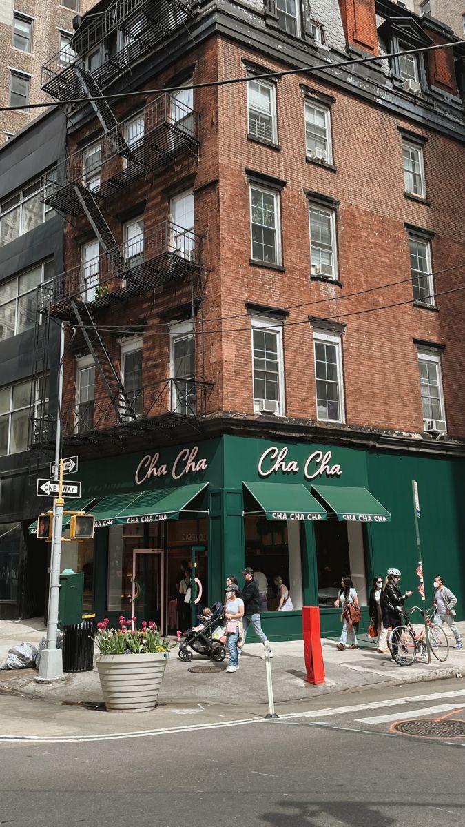 people are walking on the sidewalk in front of an old brick building with green awnings