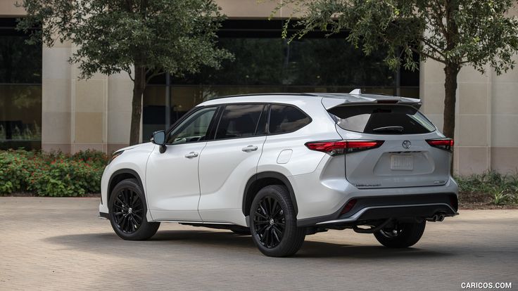 the rear end of a white toyota highland parked in front of a building with trees