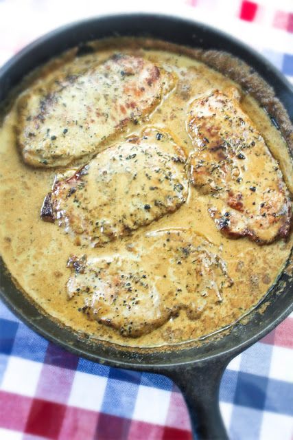 some meat is cooking in a skillet on a checkered tablecloth with a red and white napkin