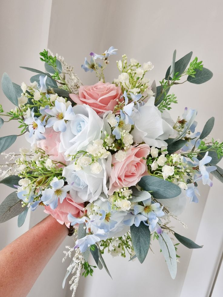 a bridal bouquet with blue and pink flowers on the bride's arm in front of a white wall