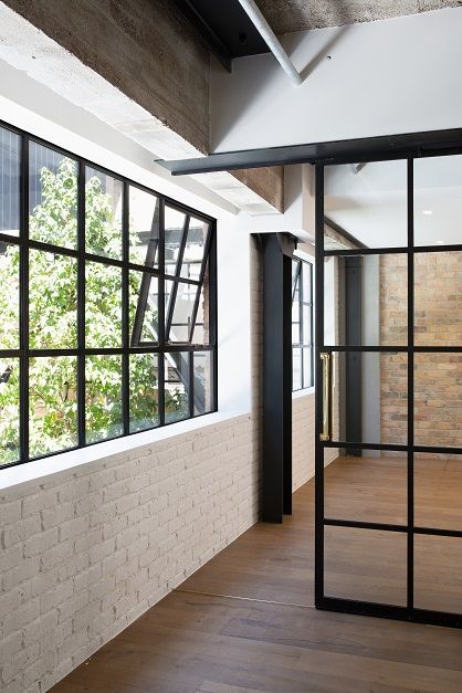 an empty room with large windows and wooden floors in front of the window is a brick wall