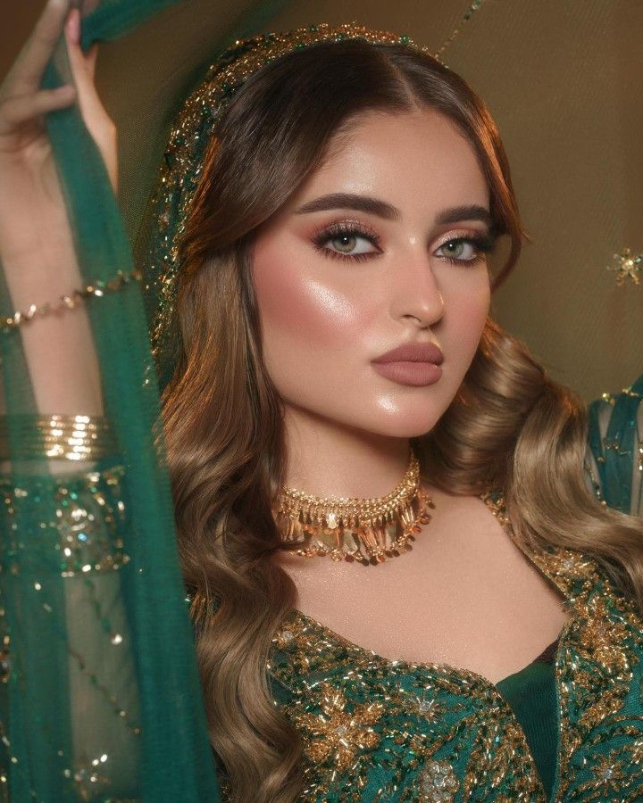 a woman with long hair wearing a green dress and gold jewelry is posing for the camera