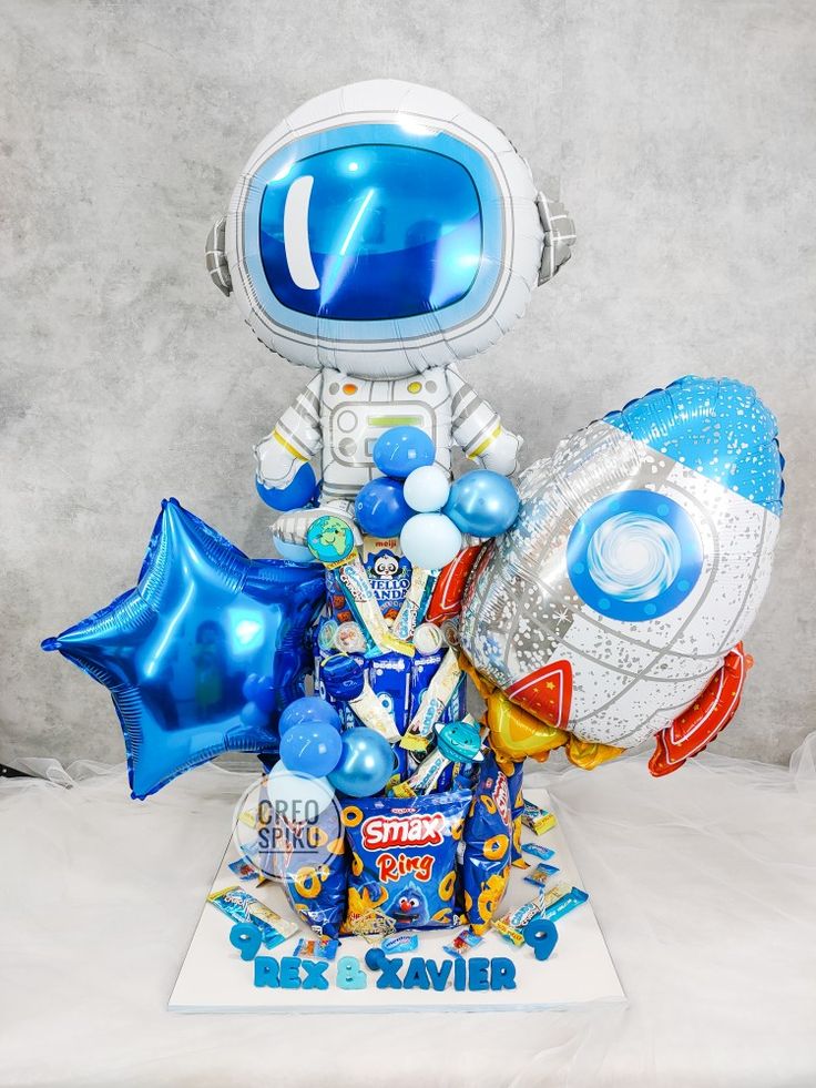 a blue and white birthday cake with an astronaut balloon on it's head, surrounded by balloons