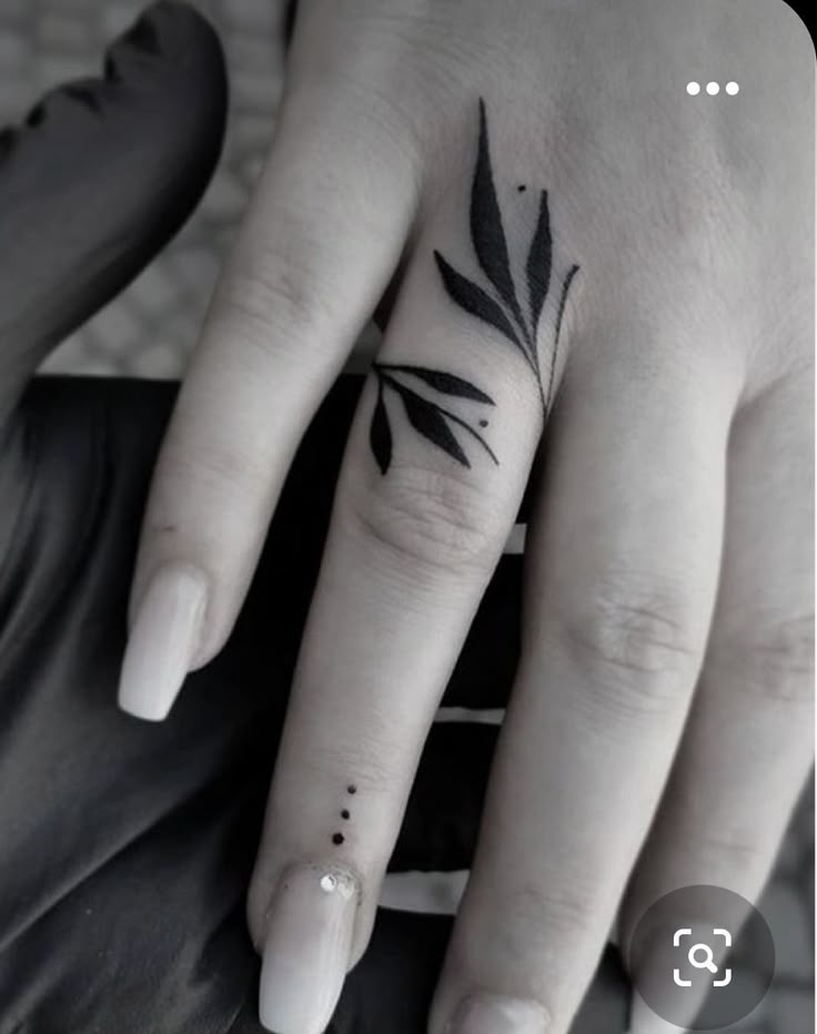 a woman's hand with a small black leaf tattoo on it