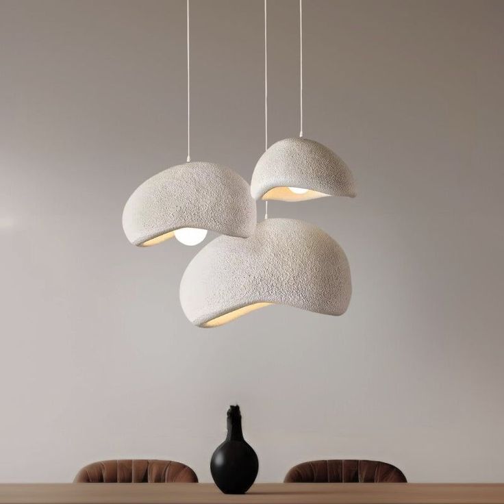 three lights hanging from the ceiling above a table with two chairs and a vase on it