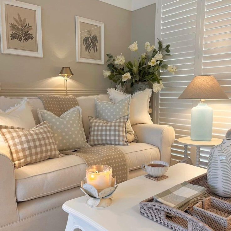 a living room filled with white furniture and flowers on top of a table in front of a window