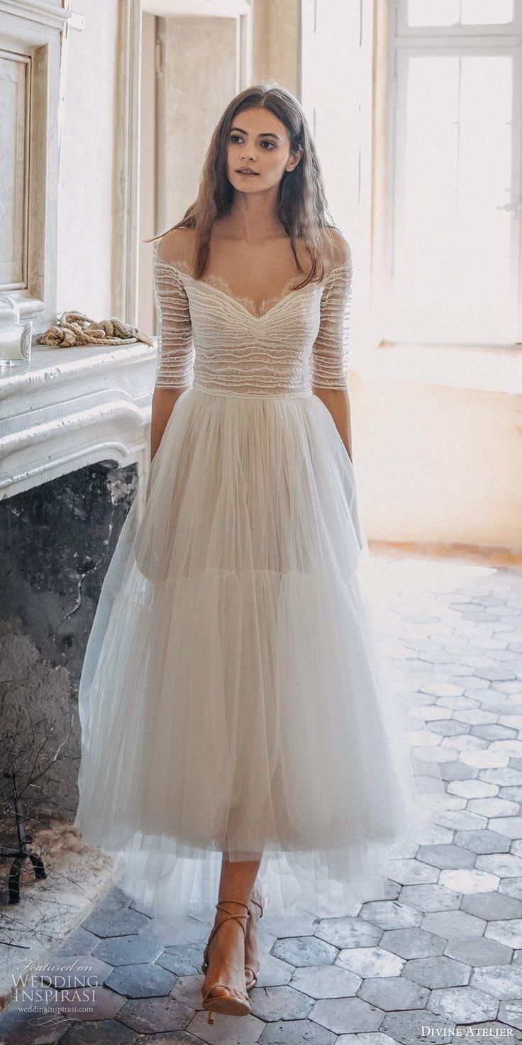 a woman in a white dress is standing near a fireplace and looking at the camera