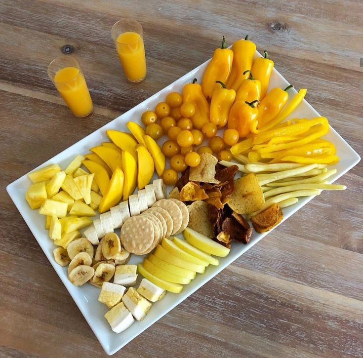 a white plate topped with different types of fruits and vegetables next to glasses of orange juice